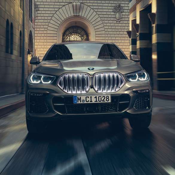 BMW X6 M50i עם גריל הכליות האייקוני המואר של BMW. BMW X6 M50i במבט קדמי בסביבה עירונית.