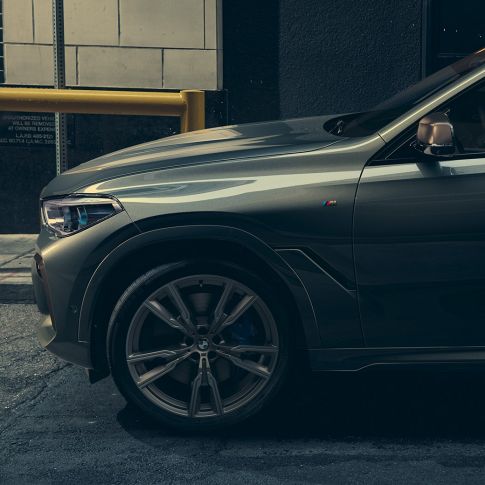 BMW X6 M50i מבט מהצד. גבר נשען על BMW X6 M50i במבט מהצד בסביבה עירונית.