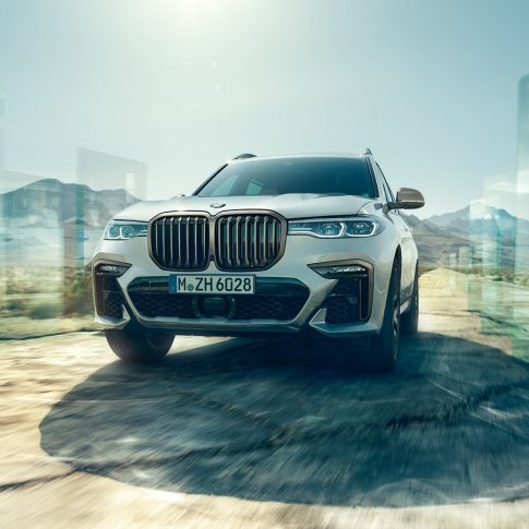 BMW X7 M50d, תצלום מזווית נמוכה BMW X7 M50d: תצלום במבט אלכסוני מזווית נמוכה על BMW X7 לבן בנסיעה