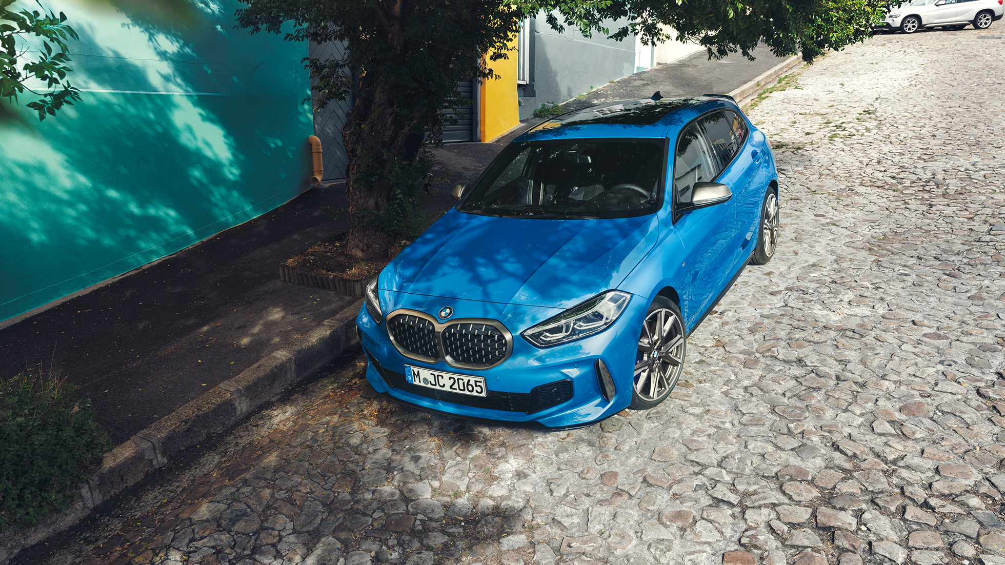 BMW סדרה 1 בצד הדרך. BMW סדרה 1 בצבע כחול מטאלי Misano blue, מבט 3/4 קדמי, חניה בצד הדרך, מבט ממעוף הציפור.
