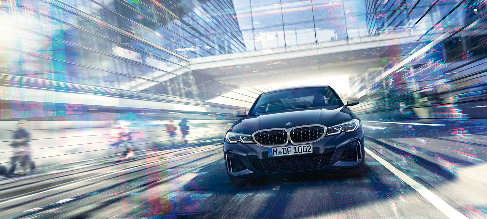BMW סידרה 3, BMW M340i xDrive במבט מהחזית. מבט על החזית של BMW M340i xDrive סדאן בנסיעה, בין מבני זכוכית עירוניים.