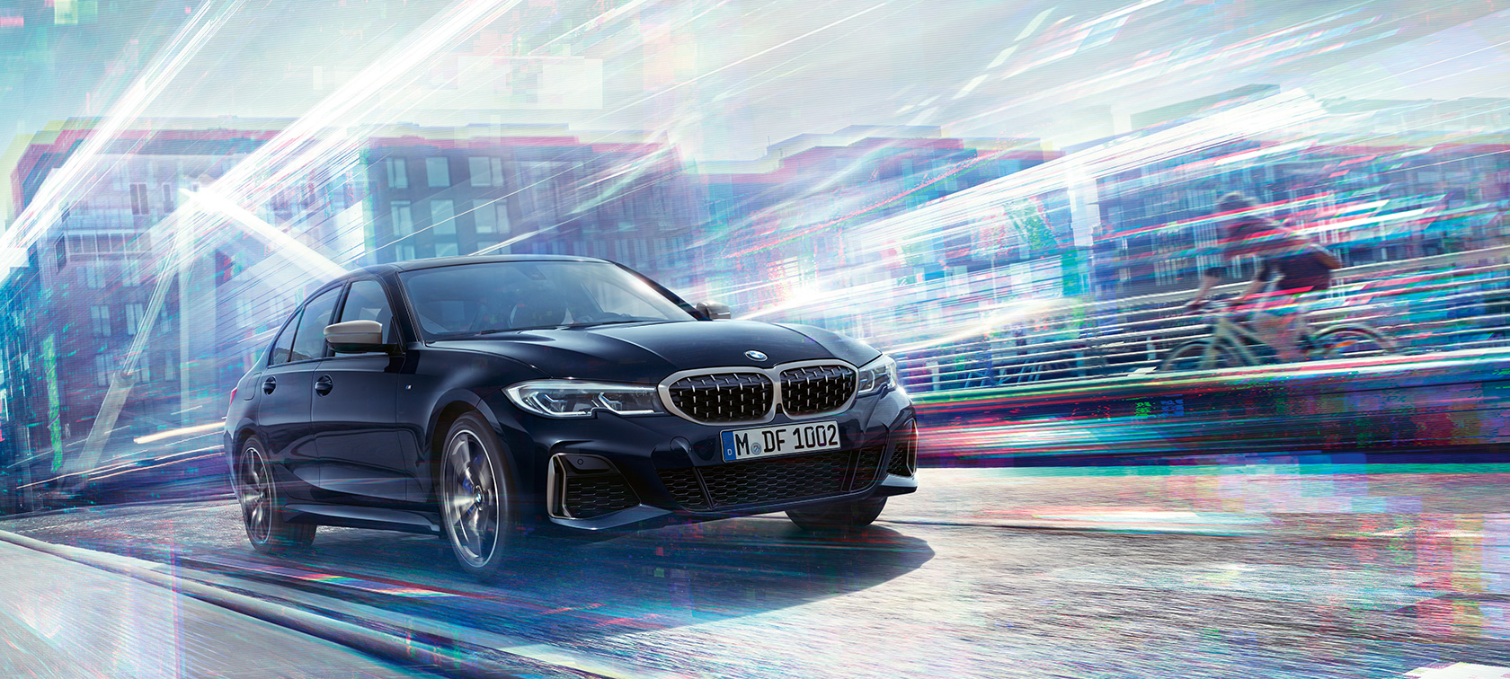 BMW סידרה 3, דגם BMW M340i xDrive. מבט אלכסון-צד על BMW M340i xDrive בנסיעה בדרך, על רקע נוף עירוני.