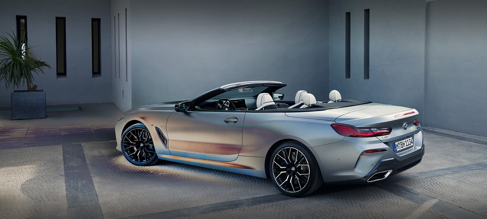 מבט צדדי BMW סדרה 8 קבריולה מתיחת פנים עומד לפני בניין אדם נשען על BMW סדרה 8 קבריולה מתיחת פנים BMW Individual Frozen Pure Grey אפור מטאלי מבט מהצד עומד לפני בניין עם אדם