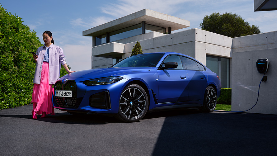 BMW i4 M50 2021 BMW Individual Frozen Portimao Blue מטאלי מבט קדמי בעמידה עם אישה לפני הבית