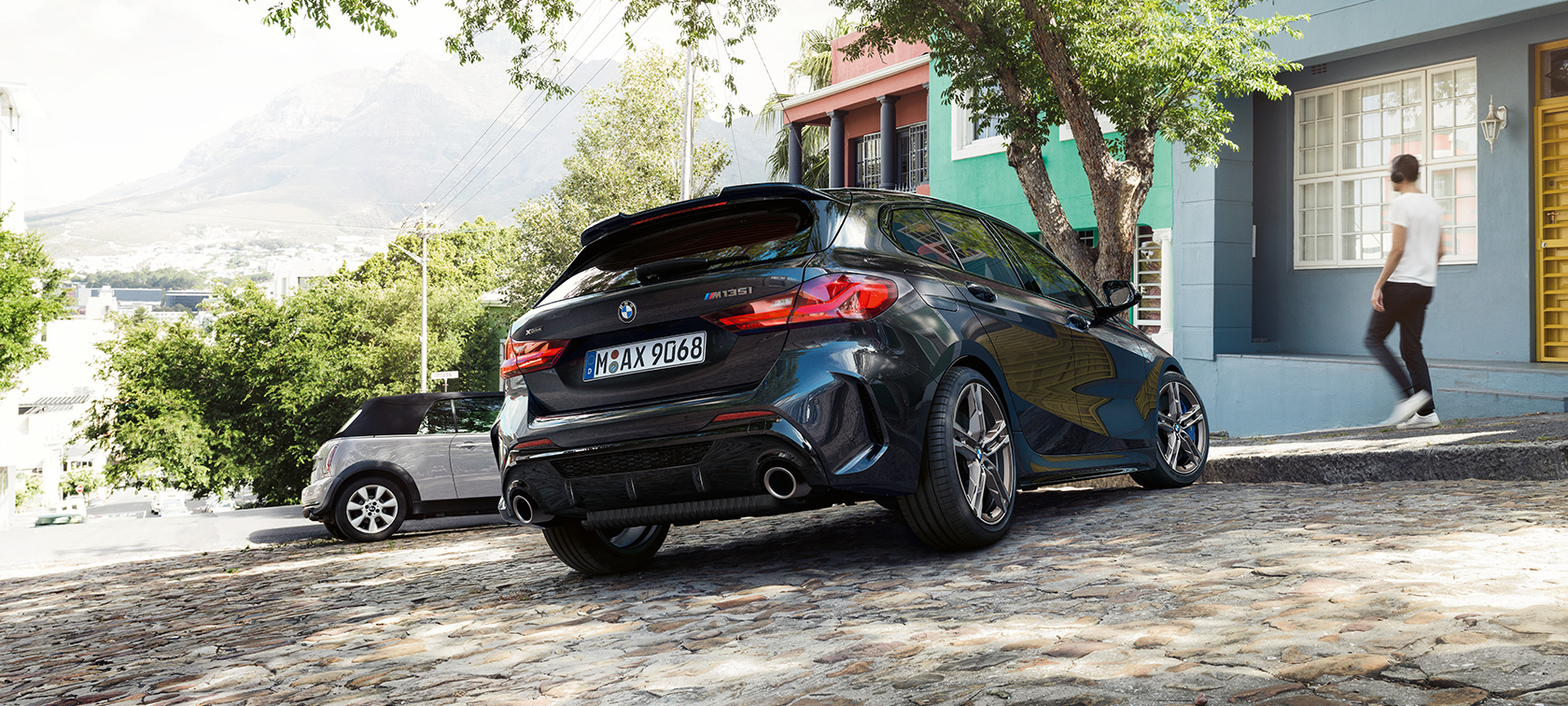 BMW M135i xDrive, מבט 3/4 אחורי ה-BMW M135i xDrive בצבע שחור מטאלי Sapphire, מבט 3/4 אחורי, לפני בניין מגורים