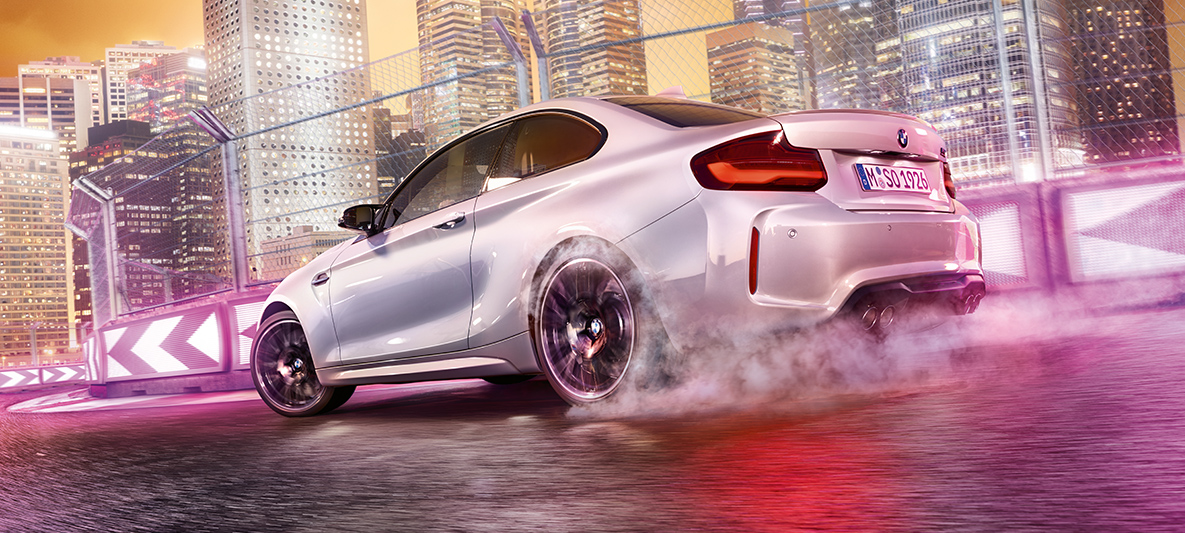BMW M2 Competition מאיצה White BMW M2 Competition drifting on race track in front of nocturnal skyline.