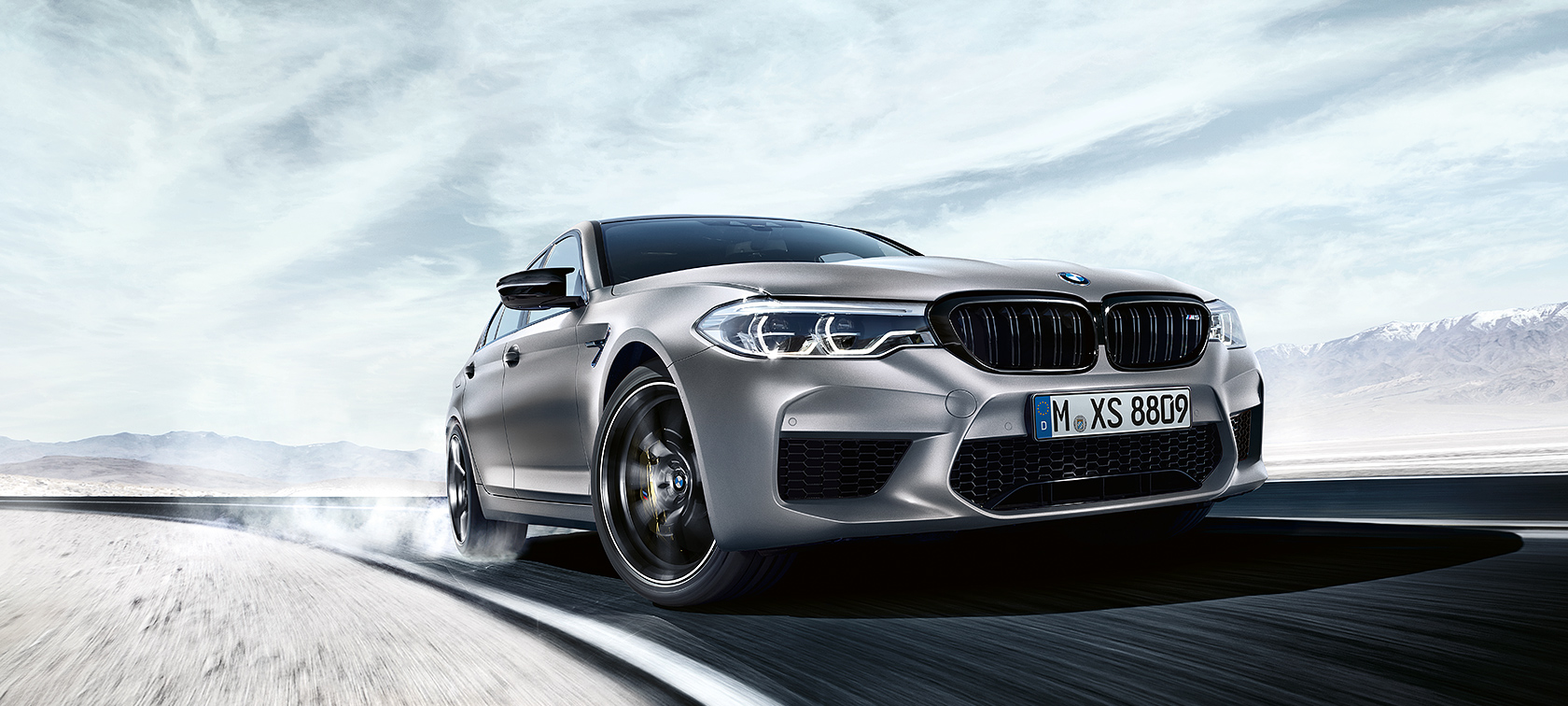 BMW M5 Competition בפעולה BMW M5 Competition בצבע Grey נוסעת בדרך מהירה, כשנופי המדבר ברקע