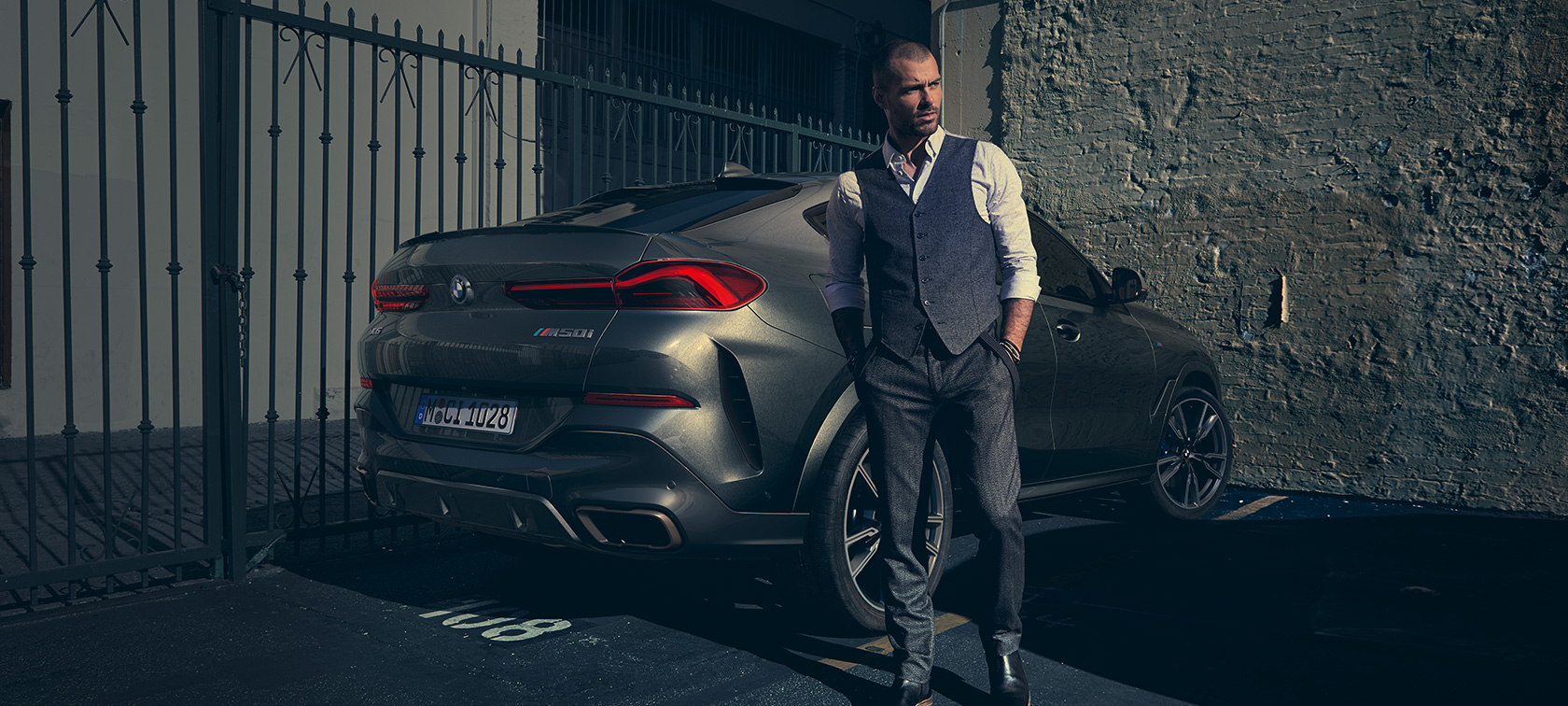 BMW X6 M50i מבט 3/4 אחורי. גבר עומד ליד BMW X6 M50i מבט 3/4 אחורי.