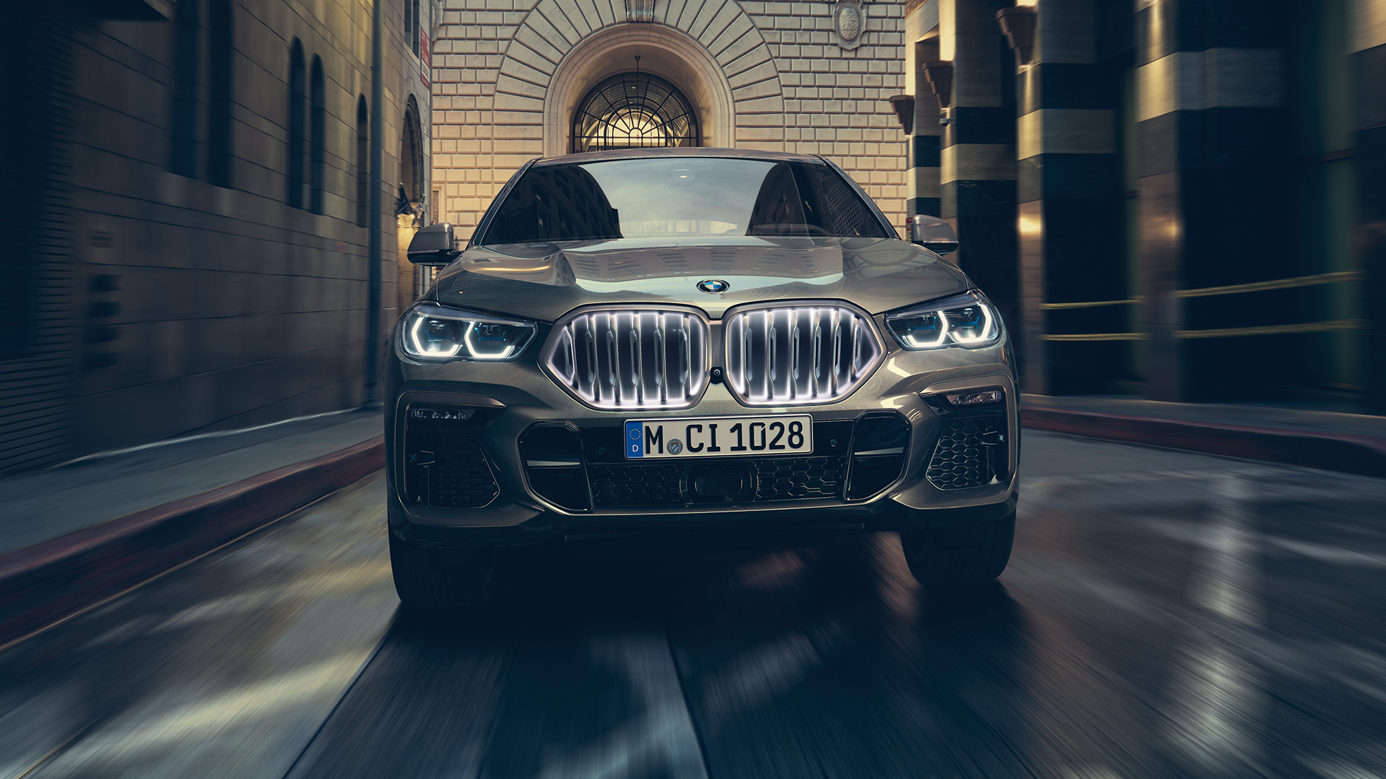 BMW X6 M50i עם גריל הכליות האייקוני המואר של BMW. BMW X6 M50i במבט קדמי בסביבה עירונית.