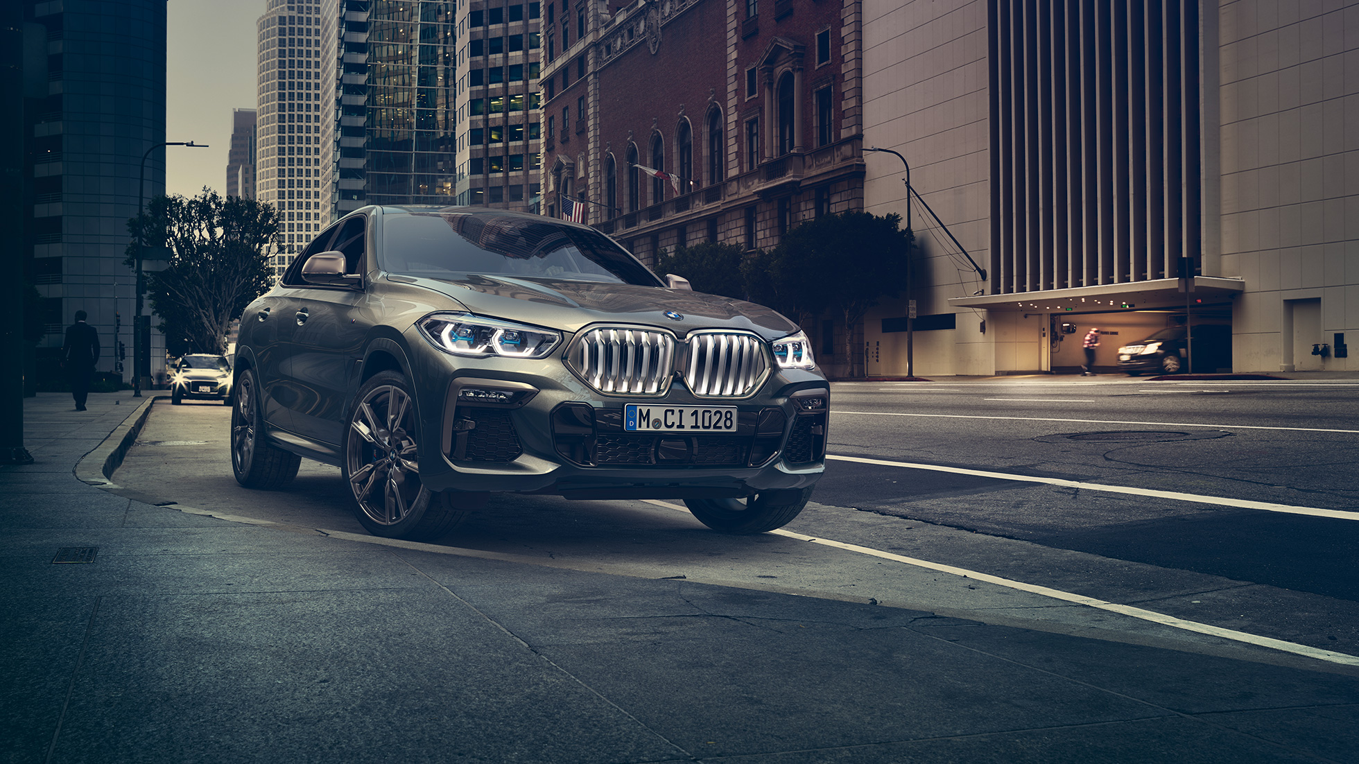 BMW X6 M50i עומד. BMW X6 M50i, מבט 3/4 קדמי בעמידה לפני תמונת נוף עירוני.