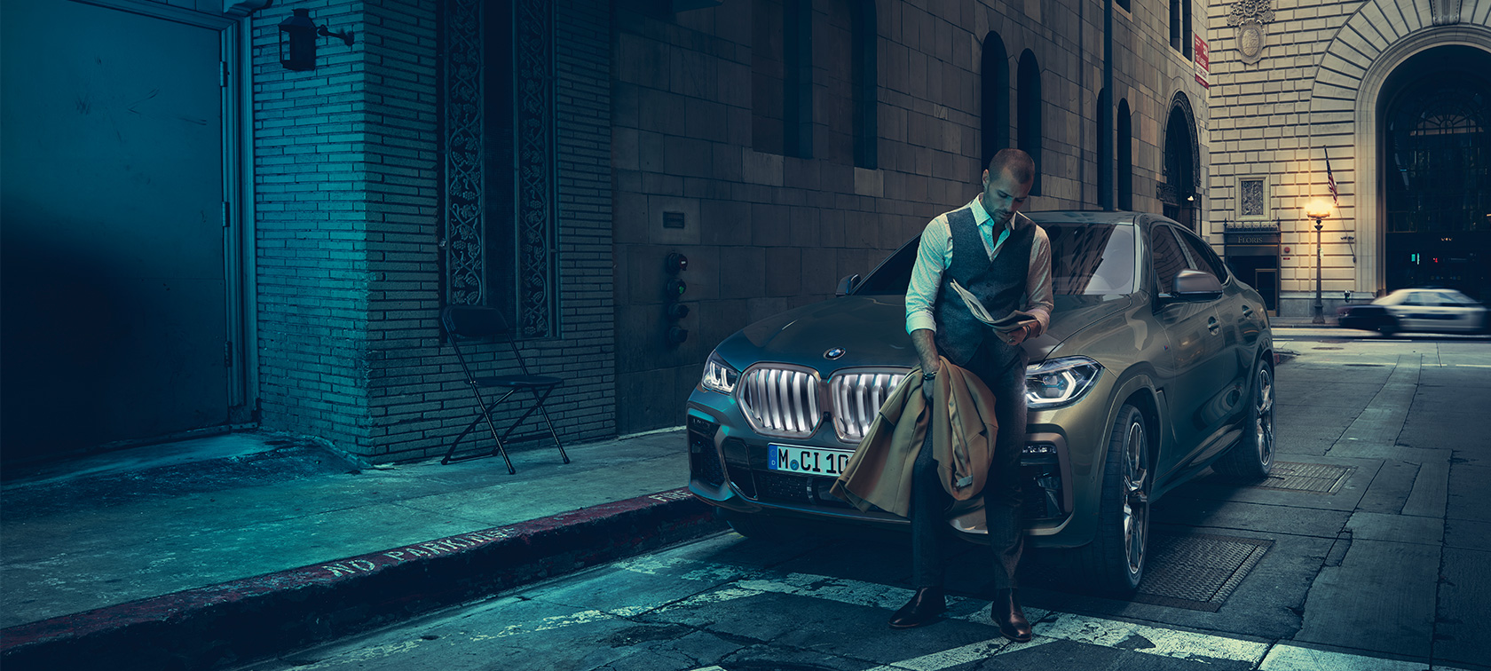 חלקו הקדמי של ה-BMW X6 M50i. גבר נשען על חלקו הקדמי של ה-BMW X6 M50i.