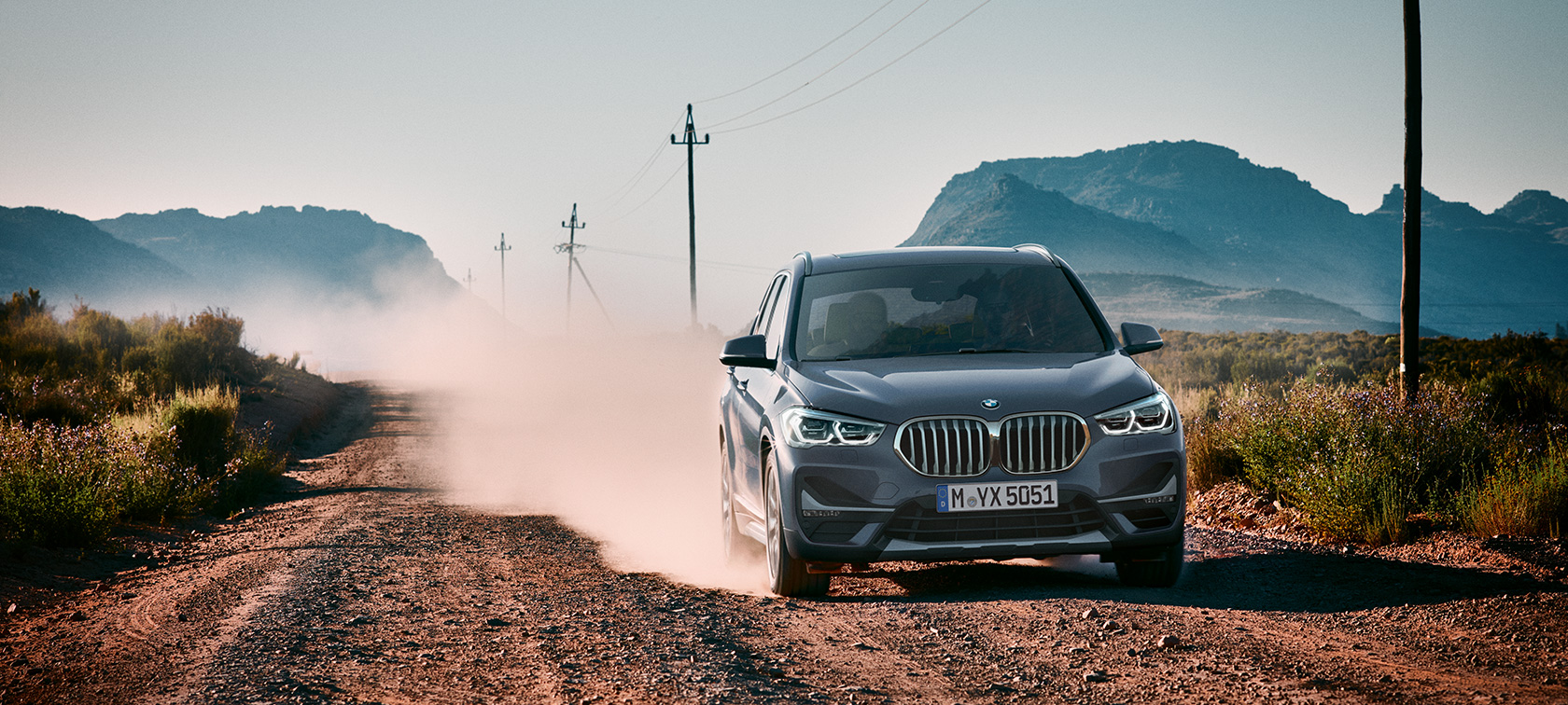 BMW X1, מבט 3/4 אחורי. BMW X1, מבט 3/4 אחורי בנסיעה לפני תמונת נוף הררי.