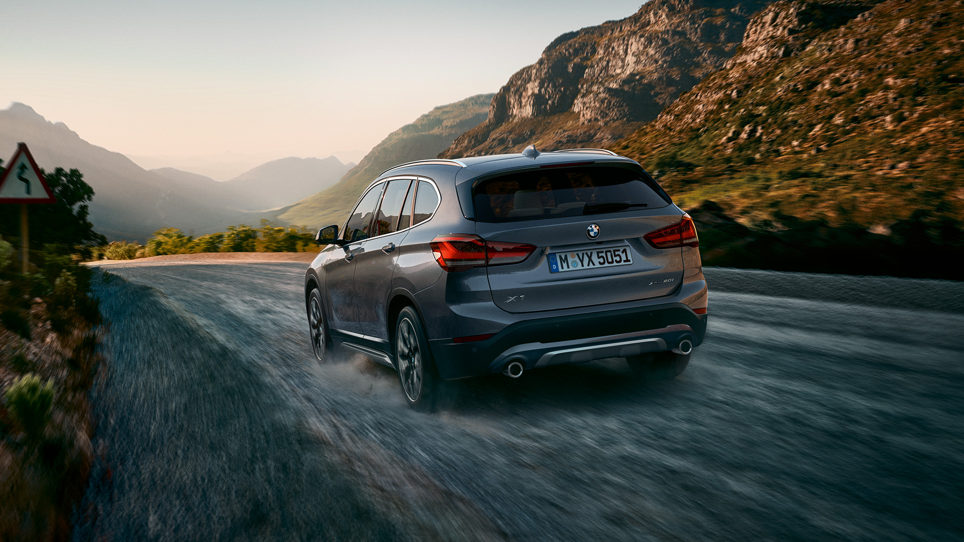 BMW X1, מבט 3/4 אחורי. BMW X1, מבט 3/4 אחורי בנסיעה לפני תמונת נוף הררי.