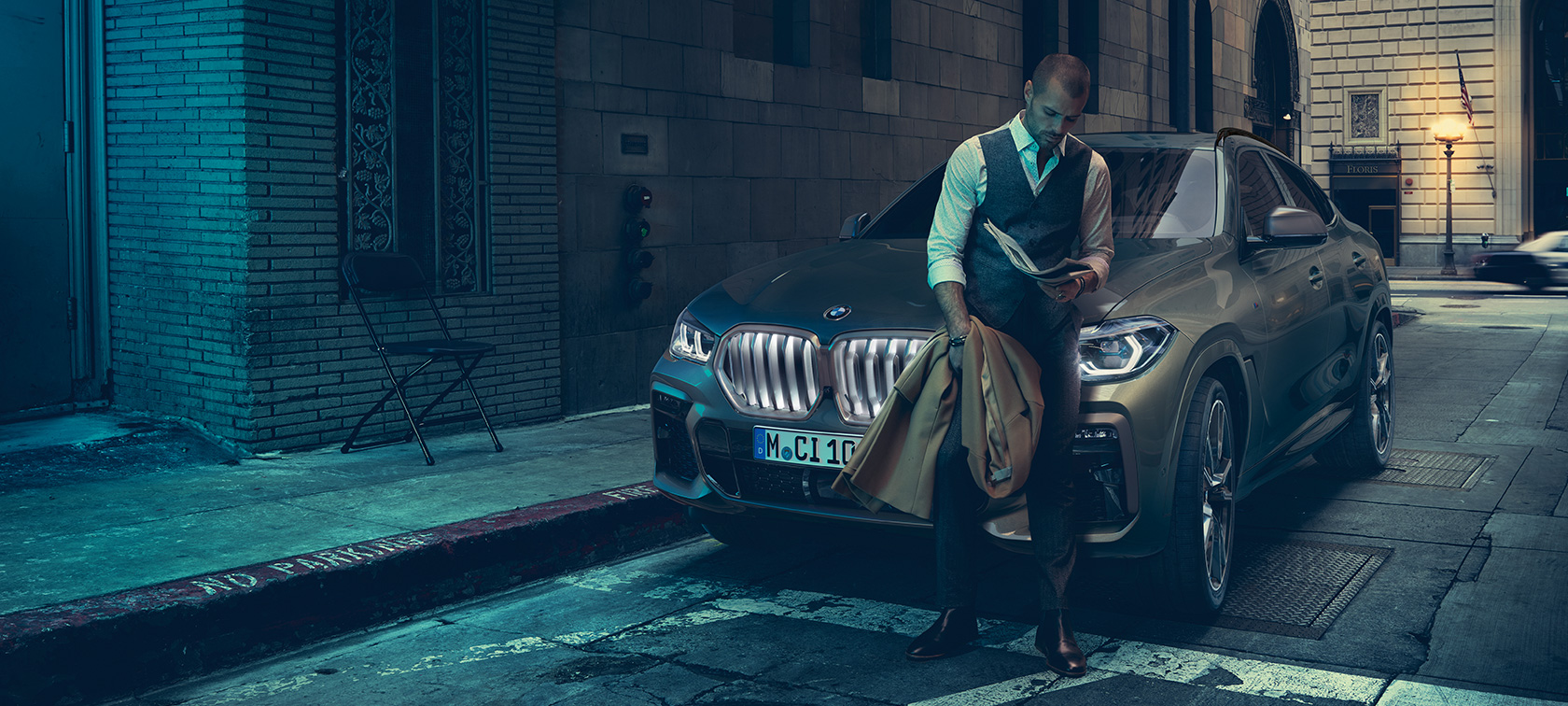 גבר נשען על BMW X6. Man leaning on BMW X6 in lateral perspective in front of an urban setting.