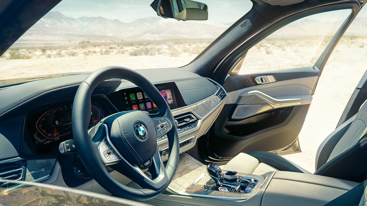 תא הנוסעים של BMW X7 תא הנוסעים של BMW X7: מבט מבחוץ על שורת המושבים הראשונה, שמציג את גלגל ההגה, לוח המחוונים ומושבי העור